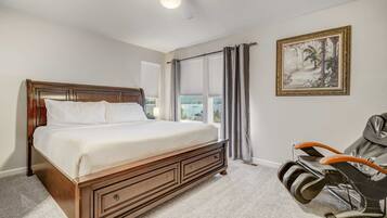A bedroom with a large bed, a massage chair, a ceiling fan, and a window with curtains.