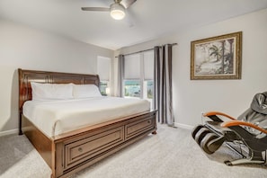 Une chambre à coucher avec un grand lit, un fauteuil massant, un ventilateur de plafond et une fenêtre avec des rideaux.
