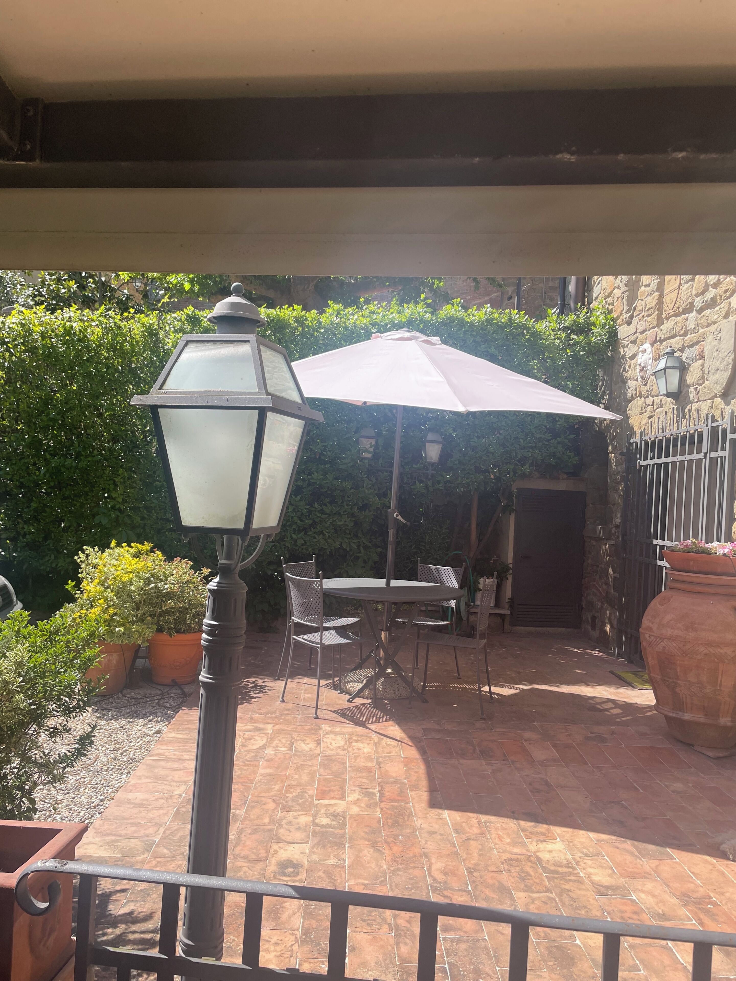 Une terrasse avec une table et des chaises, un lampadaire et un grand parasol.