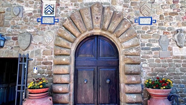 A stone building with a dark wooden door, two large terracotta pots with flowers, and stone plaques with inscriptions. - XIV Century Nest in Ancient Palagio - Montecatini Alto (Montecatini Alto)