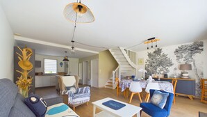 Een moderne woonkamer met een bank, salontafel en stoelen. Er is een eethoek met een tafel en stoelen. Een trap leidt naar een ander niveau.