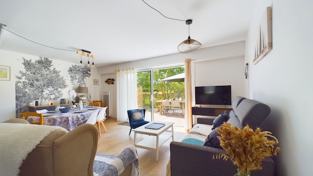 Een moderne woonkamer met een bank, een salontafel en een televisie. Er is een eethoek met een tafel en stoelen.
