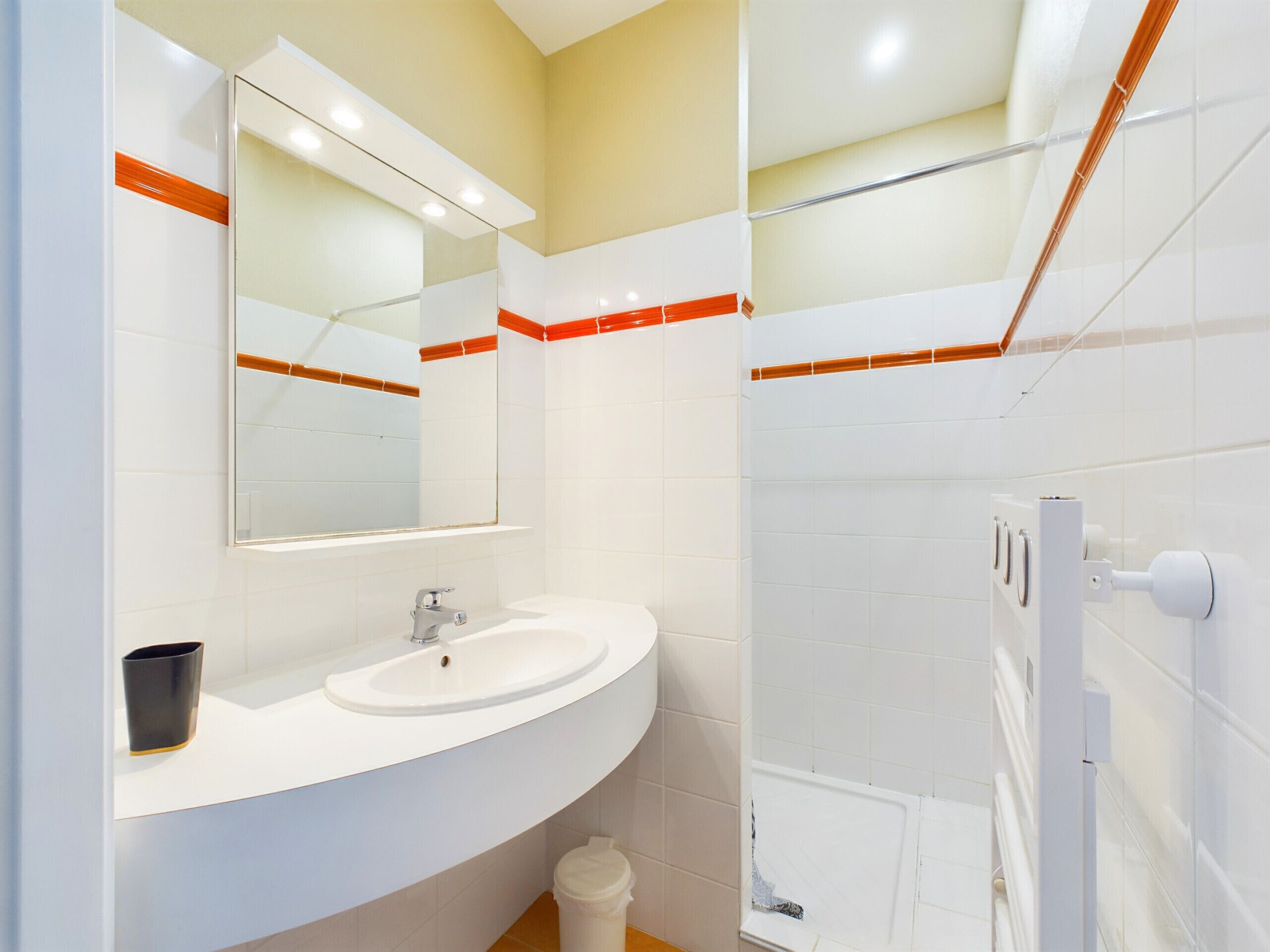 Une salle de bain moderne avec un lavabo blanc, un miroir et un espace douche.