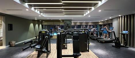Ett modernt gym med olika typer av träningsutrustning, inklusive löpband och styrketräningsmaskiner, samt ett trägolv.