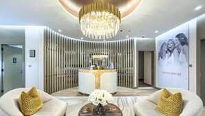 A modern lobby with a central reception desk, two sofas with gold cushions, a round coffee table with a vase, and a large chandelier. - Rooftop pool-2BR Apartment Near Downtown (Dubai)