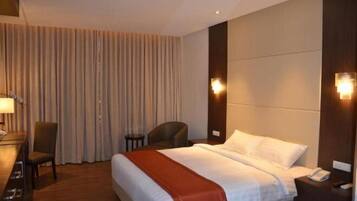 A hotel room with a bed, bedside table, lamp, chair, and curtains.