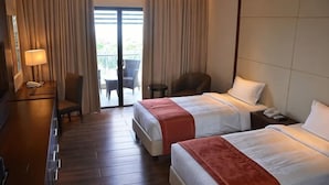 A hotel room with two beds, a desk with a lamp, a chair, and a view of the outdoors through a sliding door. - Hotel Monticello Tagaytay (Tagaytay)