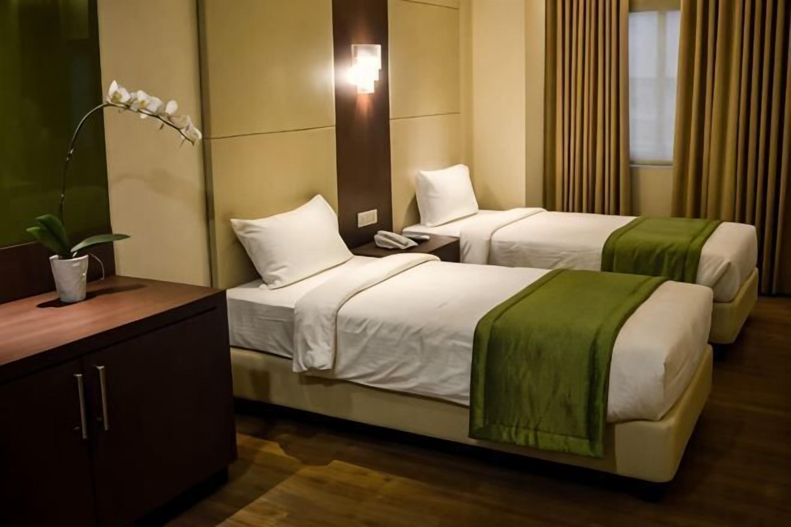 A hotel room with two beds, a bedside table, a lamp, and a potted plant.