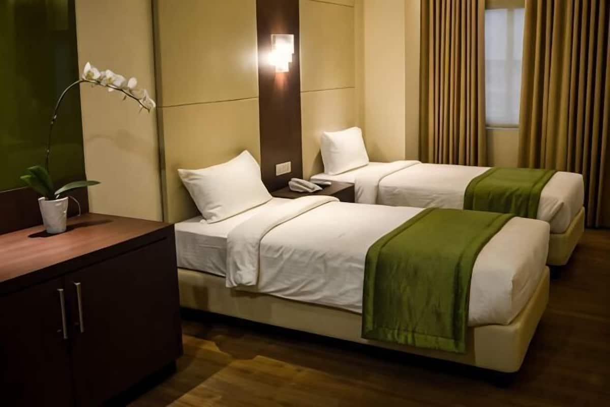 Ein Hotelzimmer mit zwei Betten, einem Nachttisch, einer Lampe und einer Zimmerpflanze.