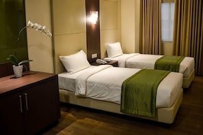 Ein Hotelzimmer mit zwei Betten, einem Nachttisch, einer Lampe und einer Zimmerpflanze.