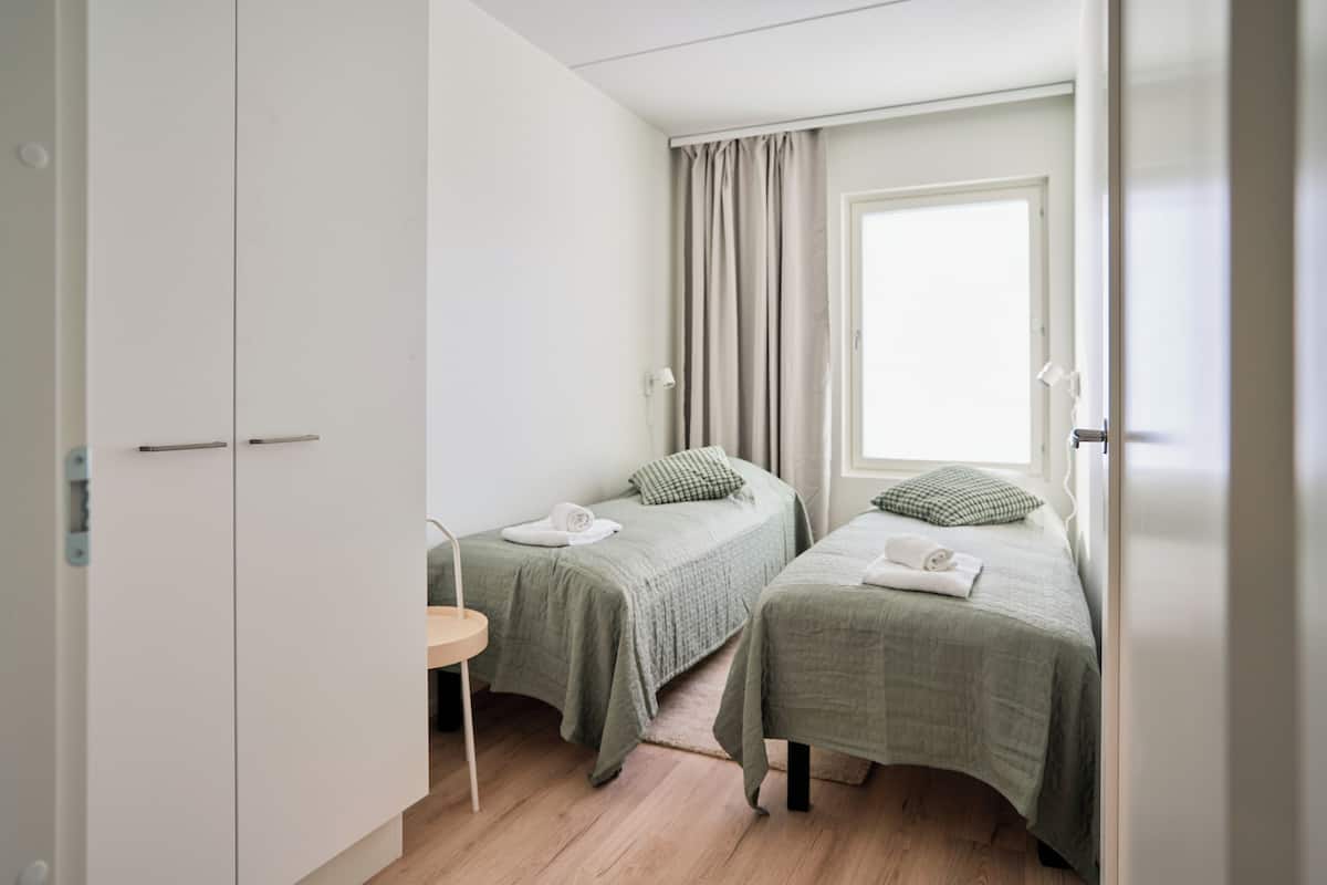 Un dormitorio con dos camas individuales, una mesita pequeña y un armario.