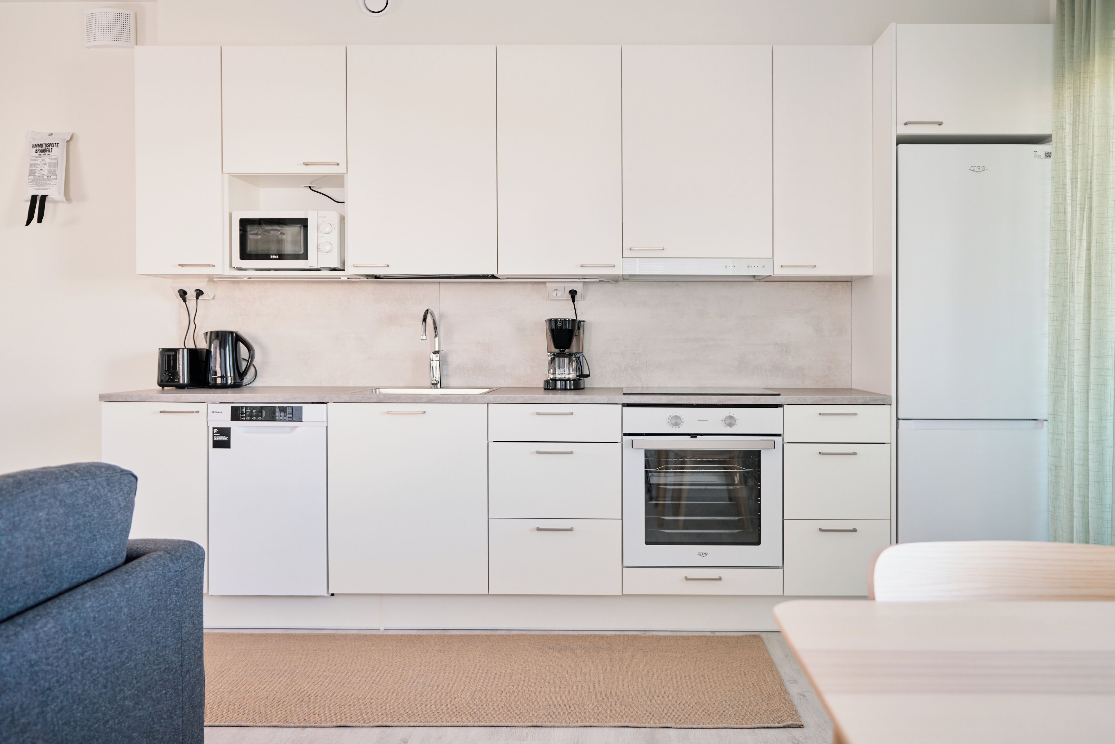 A modern kitchen with white cabinets, a microwave, a coffee maker, a dishwasher, and an oven.