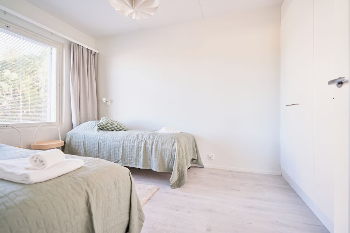 Un dormitorio con dos camas, una ventana con cortinas, una mesita de noche y un armario.