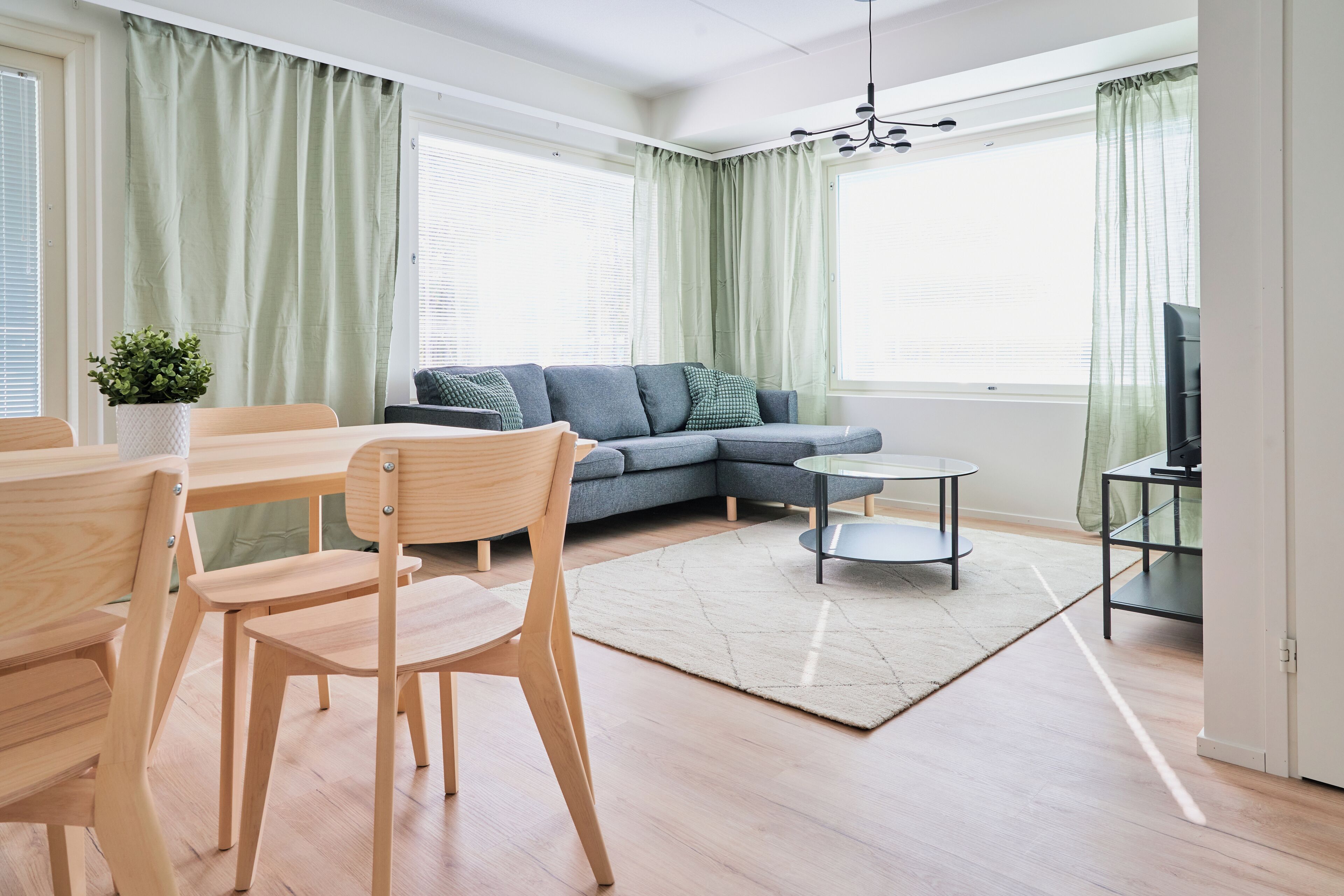 Una sala de estar moderna con un sofá modular, una mesa de comedor con sillas, una mesa de centro y un televisor sobre un mueble.
