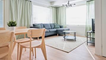 Una sala de estar moderna con un sofá modular, una mesa de comedor con sillas, una mesa de centro y un televisor sobre un mueble.