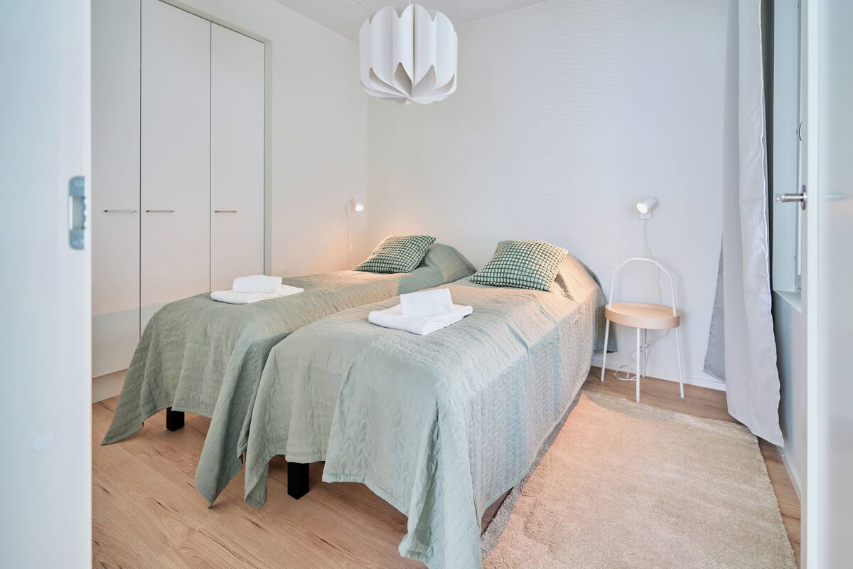 Un dormitorio moderno con dos camas, un armario blanco, una lámpara colgante y una mesita de noche pequeña.