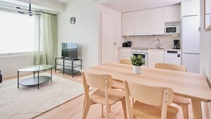A modern kitchen with white cabinets, a microwave, and a coffee maker. There is a dining table with chairs and a small round table with a glass top. - Forenom Serviced Apartments Klaukkala (Nurmijärvi)