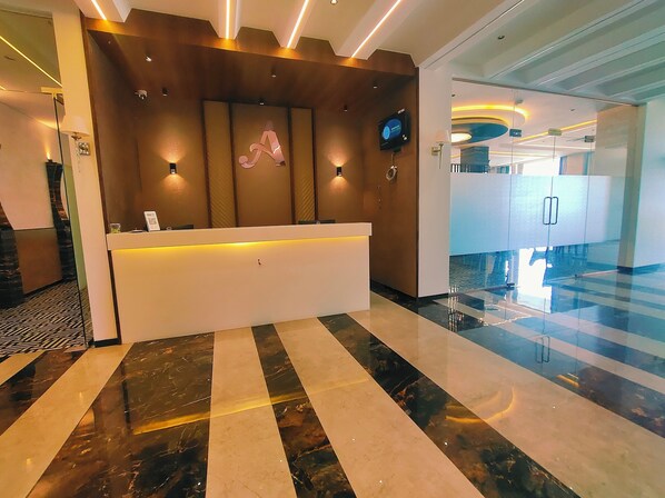A hotel reception area with a modern design, featuring a reception desk, a digital screen, and a decorative wall with a large letter 'A'. - Hotel Akshay Palace (Ahmednagar)
