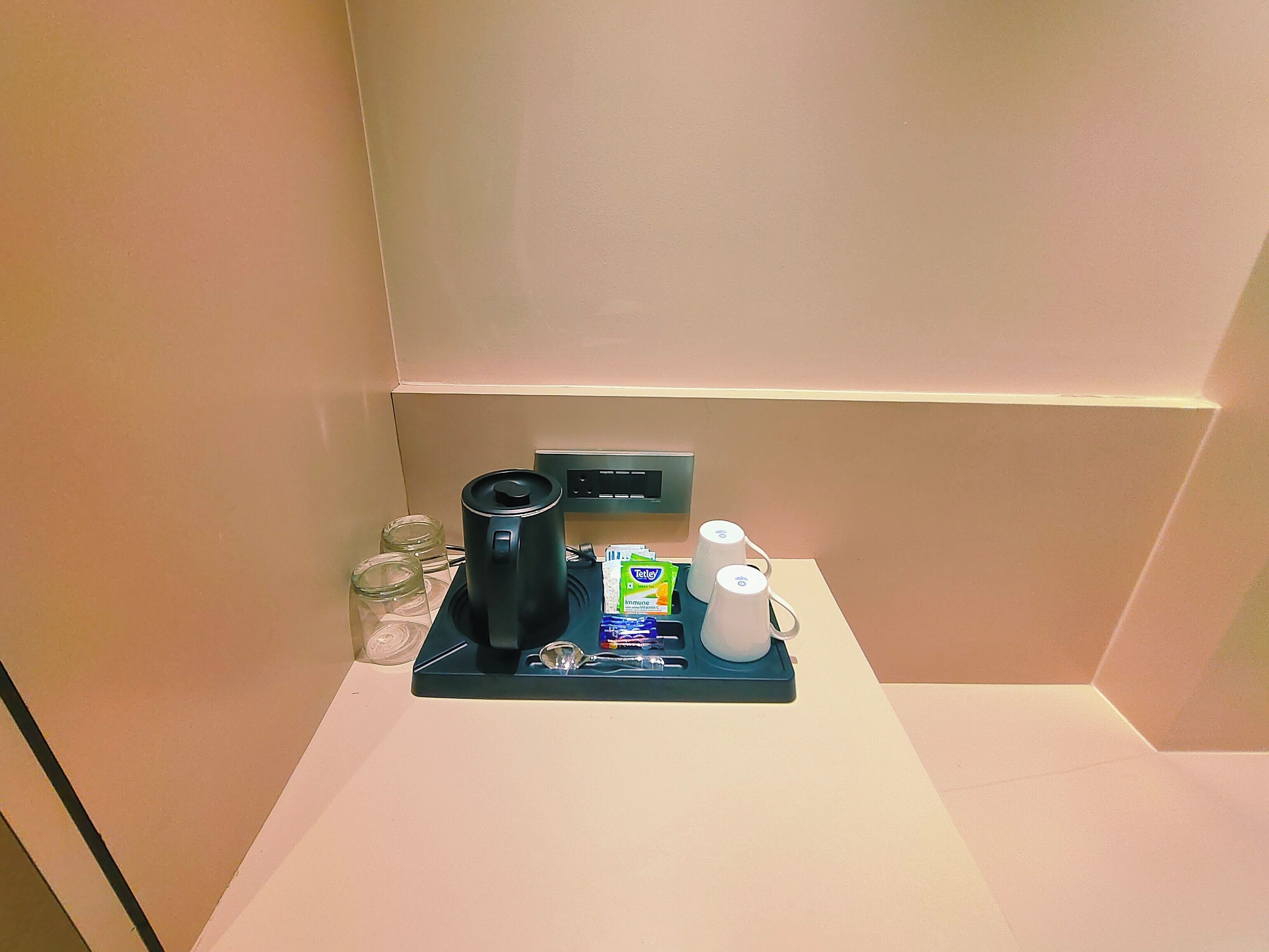 A small kitchenette with a coffee maker, a kettle, a coffee pod dispenser, and a water pitcher on a tray.