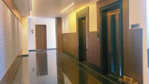 A hotel hallway with a shiny black floor, wooden panel walls, and a door with a vertical striped pattern. - Hotel Akshay Palace (Ahmednagar)