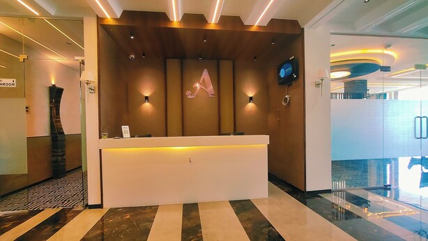 A hotel reception area with a modern design, featuring a reception desk, a large illuminated 'A' sign, and a polished marble floor. - Hotel Akshay Palace (Ahmednagar)