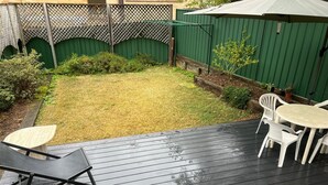 A wooden deck with a table and chairs, surrounded by a green fence and a grassy yard.