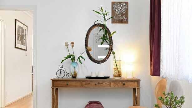 A wooden console table with a mirror, a vase with flowers, a small potted plant, a candle, and a decorative plate.