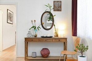 Een houten consoleschrank met een spiegel, een vaas met bloemen, een kleine potplant, een kaars en een decoratief bord.