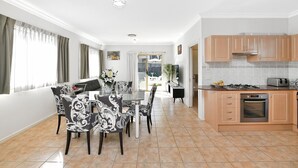 A modern kitchen with a gas stove, oven, and toaster. There is a dining area with a table and chairs, and a large window with curtains.