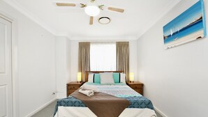 A neatly arranged bedroom with a bed, bedside lamps, a ceiling fan, and a painting on the wall.