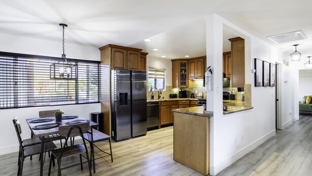 A modern kitchen with wooden cabinets, a stainless steel refrigerator, and a dining area with a table and chairs.
