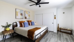 A bedroom with a bed, bedside table, nightstand, and a bench.