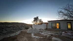 A desert landscape with a white building featuring a glass door and a stone wall.