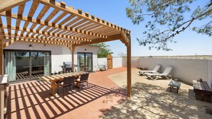 A covered patio with a wooden pergola, outdoor seating, and a view of the surrounding landscape.