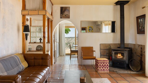 A cozy living room with a brown leather sofa, a stone fireplace, and a view through an archway to an outdoor area.
