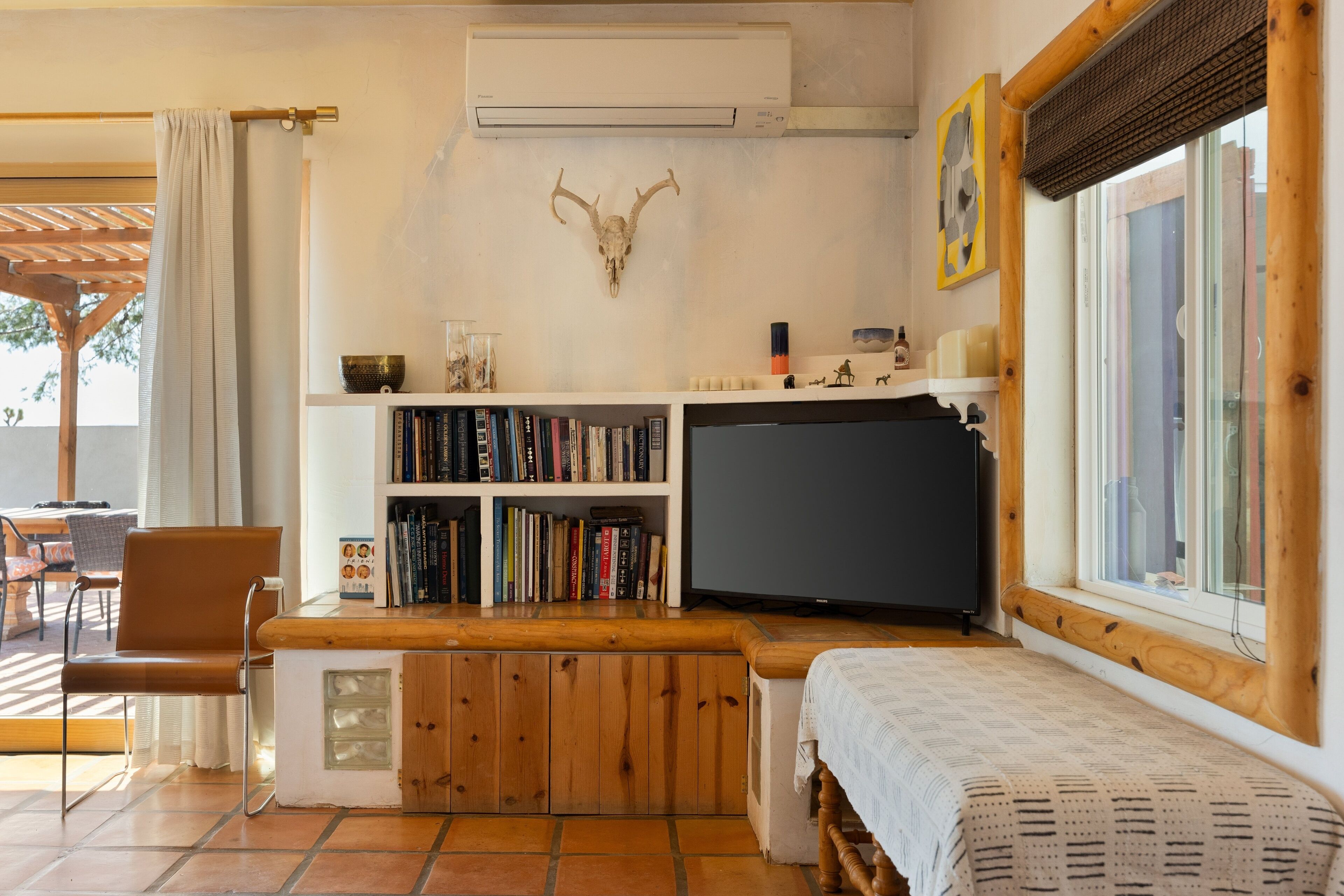 Una stanza accogliente con una panca in legno, una libreria, una televisione e un'ampia finestra.