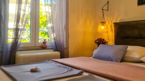 Une chambre à coucher avec un lit, une fenêtre ornée de rideaux légers, une lampe de chevet et une vue sur la verdure à l’extérieur.