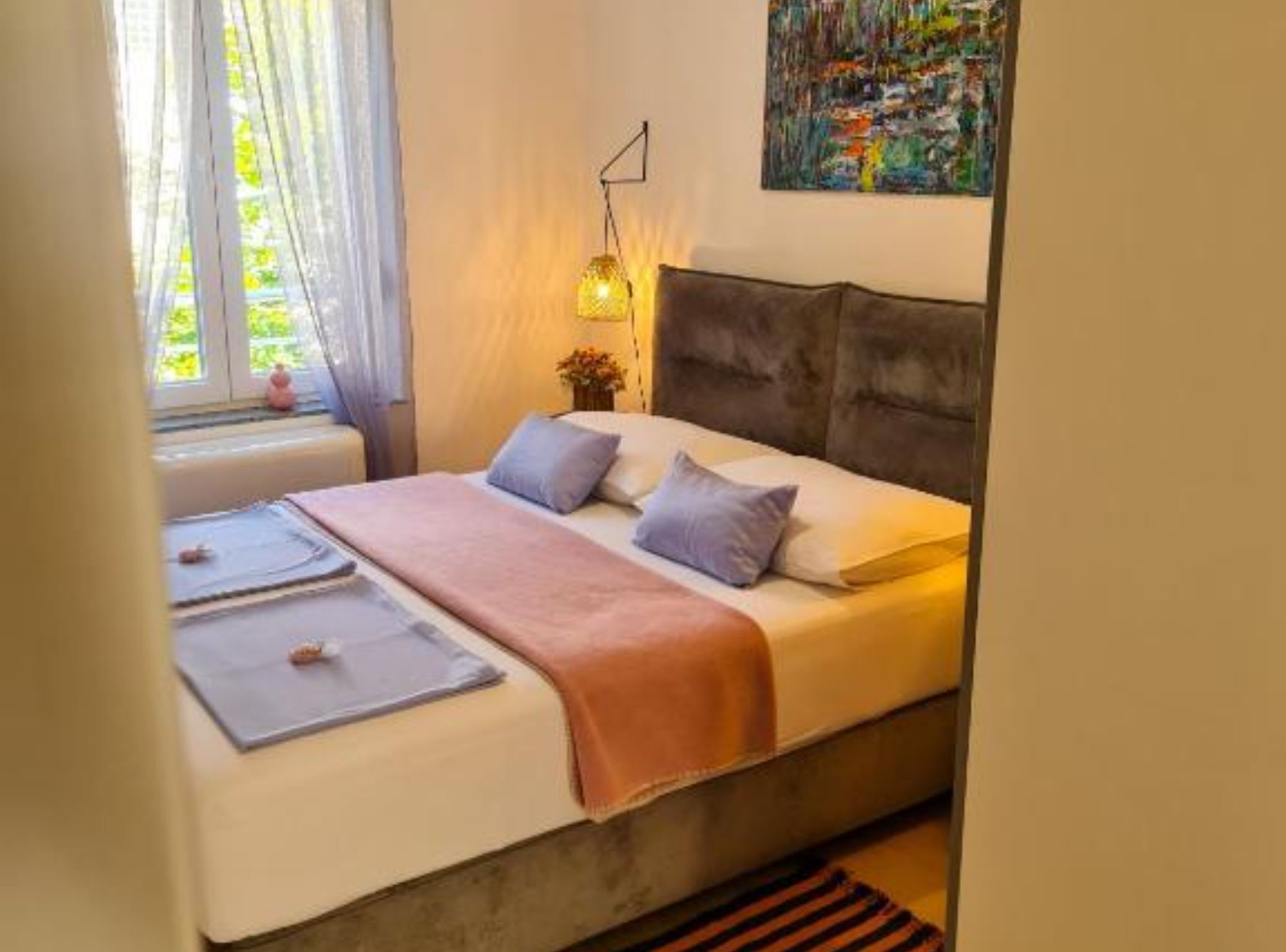 Un lit bien fait, avec une tête de lit, une table de chevet avec une lampe et une fenêtre avec des rideaux.