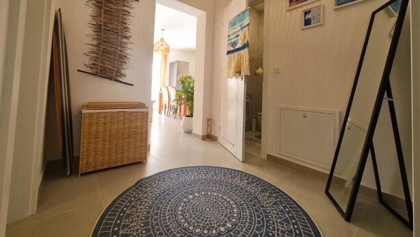 Un couloir avec un panier en osier, un tapis à motifs et un miroir appuyé contre le mur.