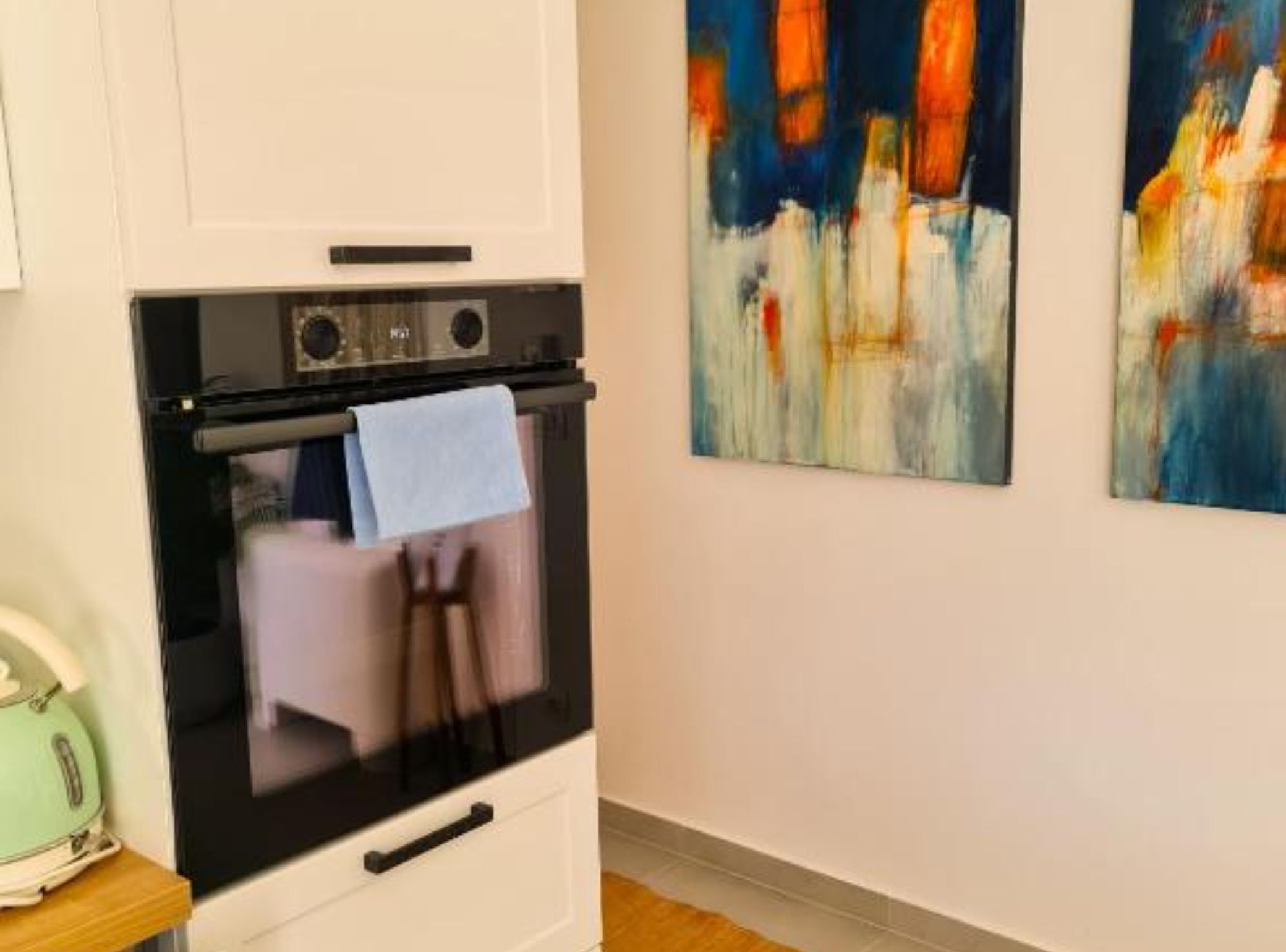 A kitchen with a built-in oven, a hanging towel, and abstract art on the wall.
