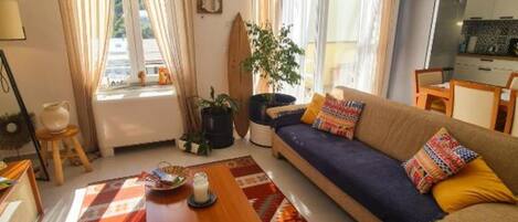 Una sala de estar con un sofá, una mesa de centro, una planta y una ventana con cortinas.