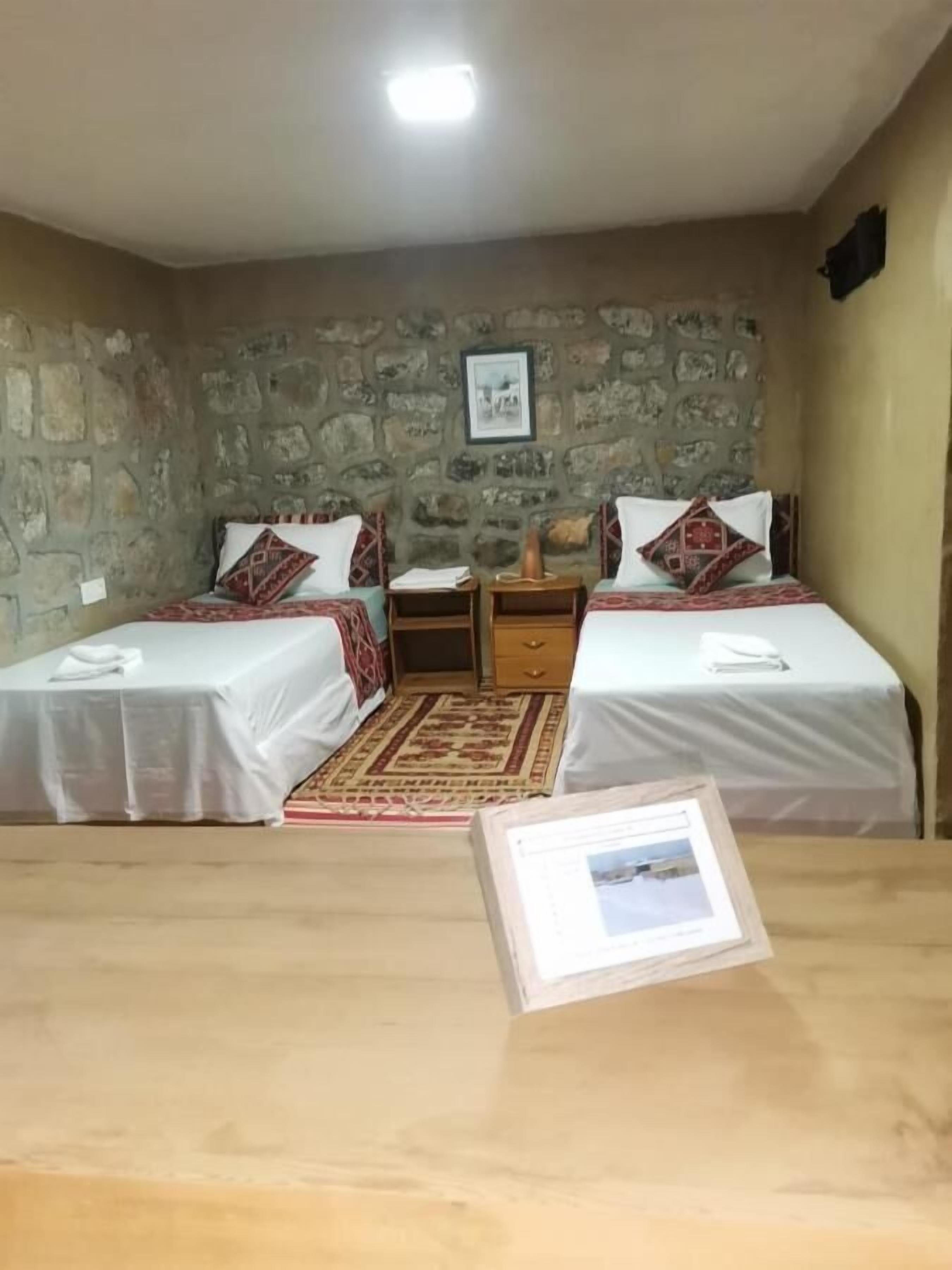 A room with two beds, a small table, and a stone wall.