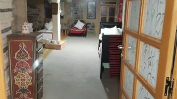 Un'ampia stanza con soffitto alto, parete in pietra, letto con coperta rossa, mobiletto in legno e porta con vetrata decorata.