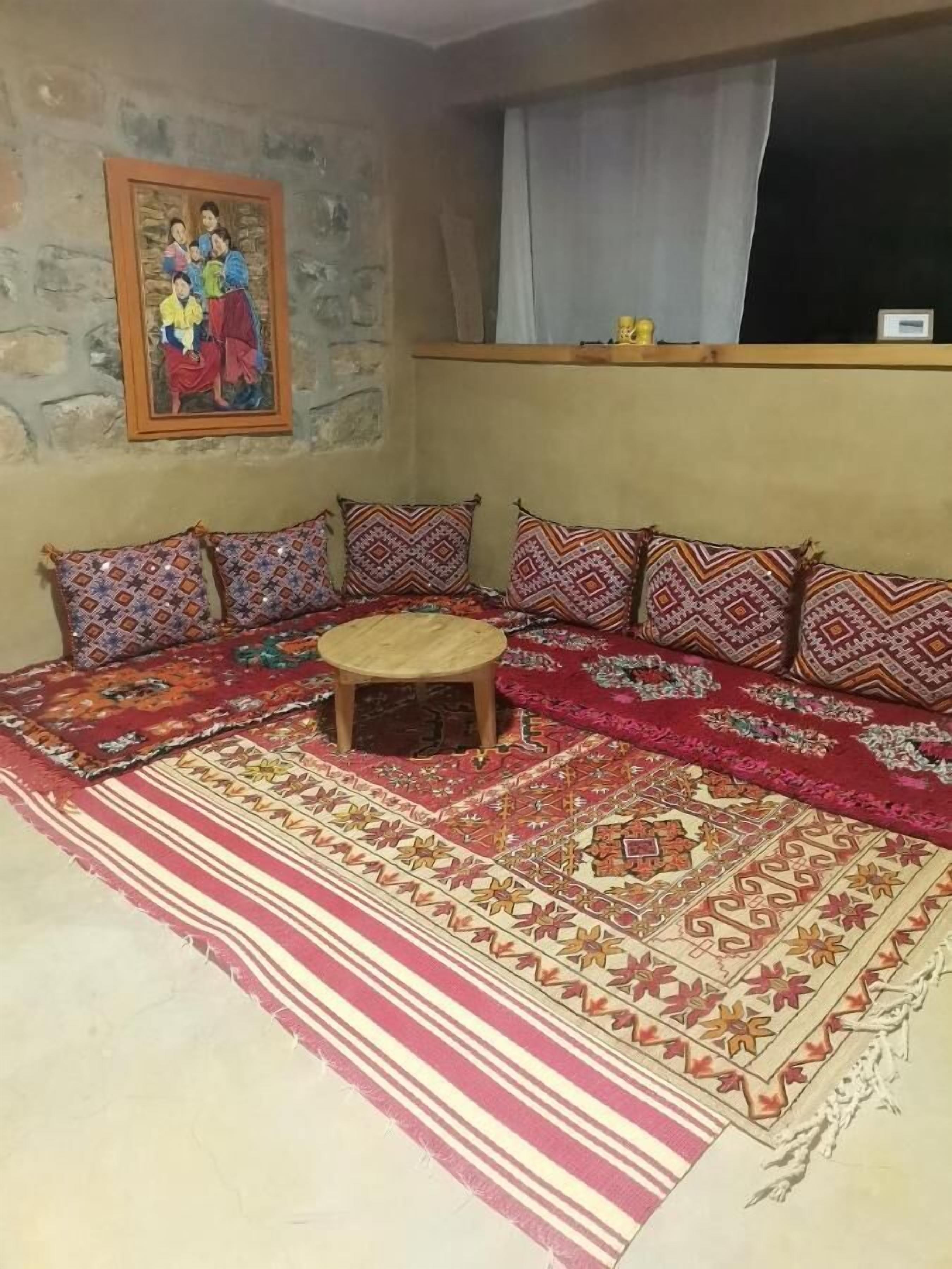 A traditional room with a stone wall, a sofa set with patterned cushions, a small wooden stool, and a large decorative rug.