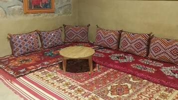 A traditional room with a stone wall, a sofa set with patterned cushions, a small wooden stool, and a large decorative rug.