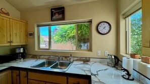 Cocina con pileta doble, armarios de madera, un reloj y ventana con vista a árboles.