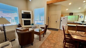 A living room with a fireplace, a television, and a dining area with a kitchen in the background. - Pet-Friendly I Rim Village I Garage I Pool & Hot Tub I Trailer Parking (Moab)