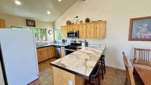 A kitchen with wooden cabinets, a marble countertop, and a dining area with a wooden table and chairs. - Pet-Friendly I Rim Village I Garage I Pool & Hot Tub I Trailer Parking (Moab)