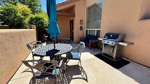 An outdoor patio with a round metal table and chairs, a blue umbrella, and a barbecue grill. - Pet-Friendly I Rim Village I Garage I Pool & Hot Tub I Trailer Parking (Moab)