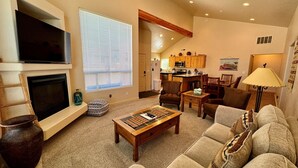 A living room with a fireplace, a television, a dining area, and a kitchen in the background. - Pet-Friendly I Rim Village I Garage I Pool & Hot Tub I Trailer Parking (Moab)